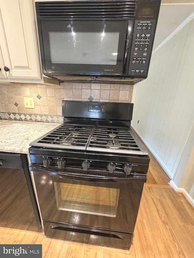 room details with light stone counters, backsplash, white cabinets, light wood-type flooring, and black appliances