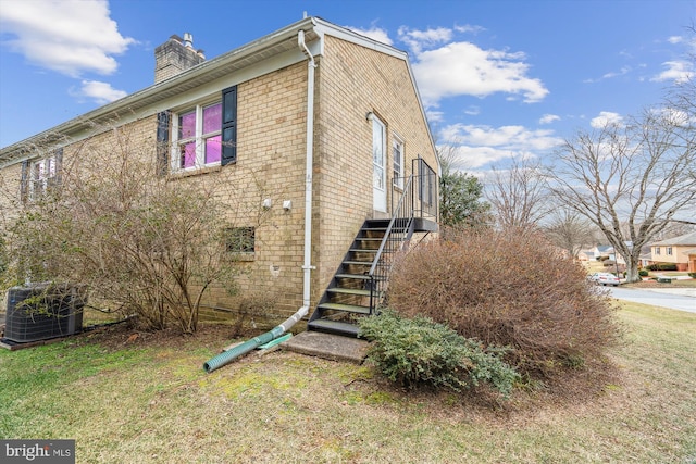 view of home's exterior with cooling unit, brick siding, stairs, a lawn, and a chimney