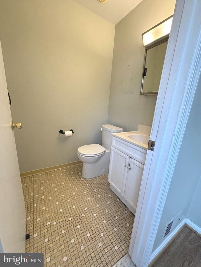 half bathroom featuring visible vents, vanity, toilet, and baseboards