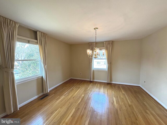 spare room featuring light wood-style floors, visible vents, baseboards, and a notable chandelier