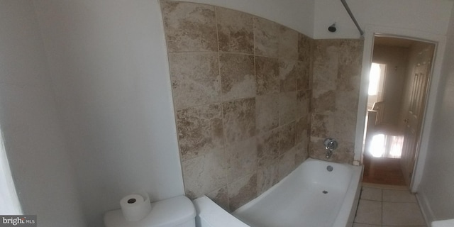 bathroom featuring tile patterned flooring, tiled shower / bath combo, and toilet