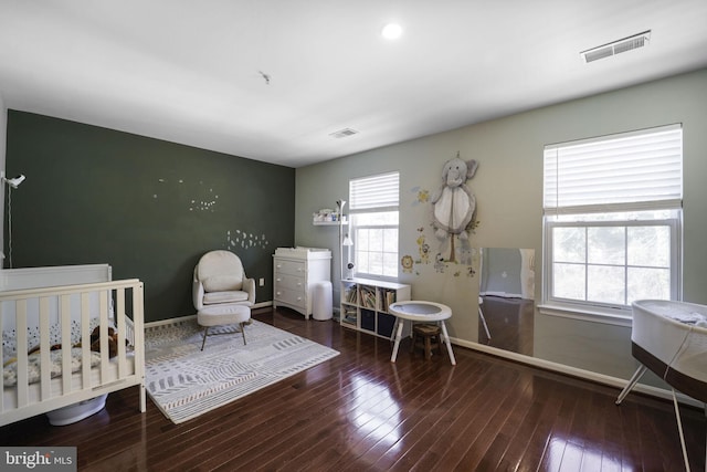 bedroom with a nursery area, baseboards, visible vents, and wood-type flooring