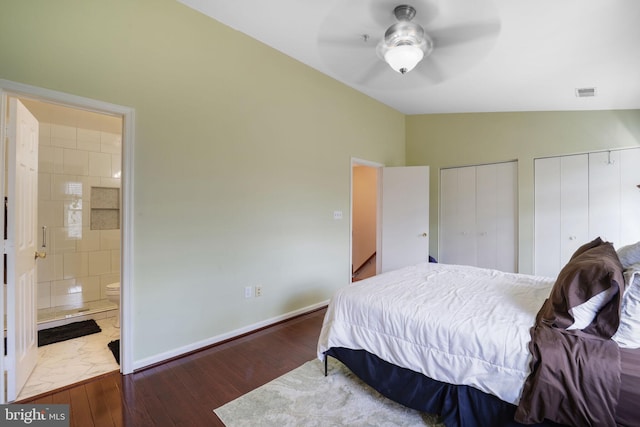 bedroom with visible vents, connected bathroom, multiple closets, vaulted ceiling, and wood finished floors