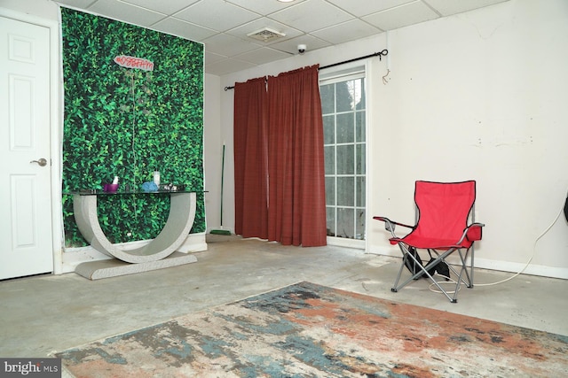 living area with a paneled ceiling and concrete flooring