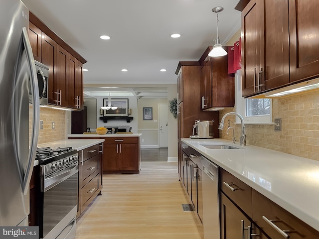 kitchen with hanging light fixtures, appliances with stainless steel finishes, sink, and light hardwood / wood-style floors