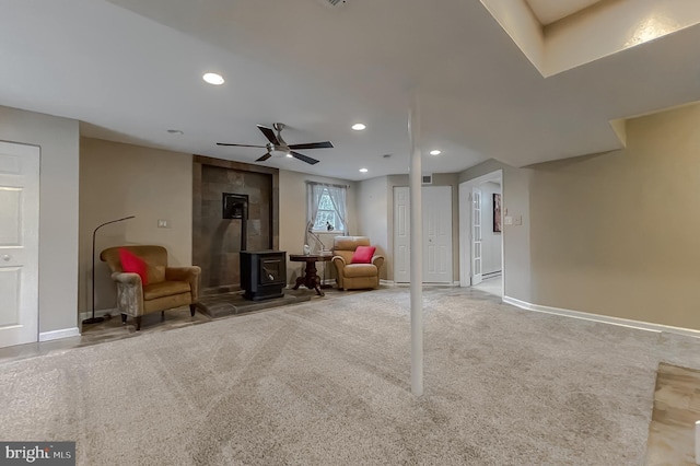 basement featuring carpet flooring, ceiling fan, and a wood stove