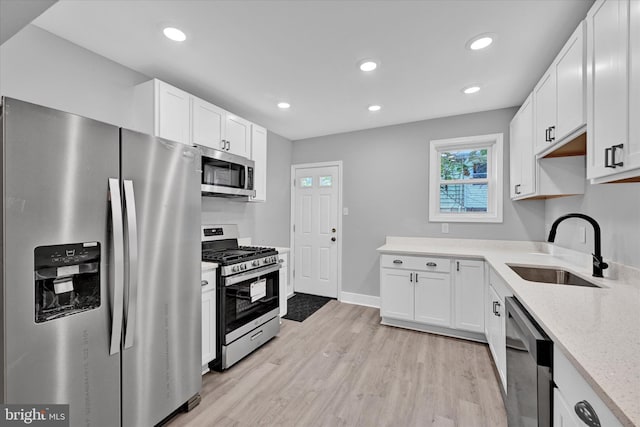 kitchen with appliances with stainless steel finishes, white cabinetry, sink, light stone counters, and light hardwood / wood-style flooring