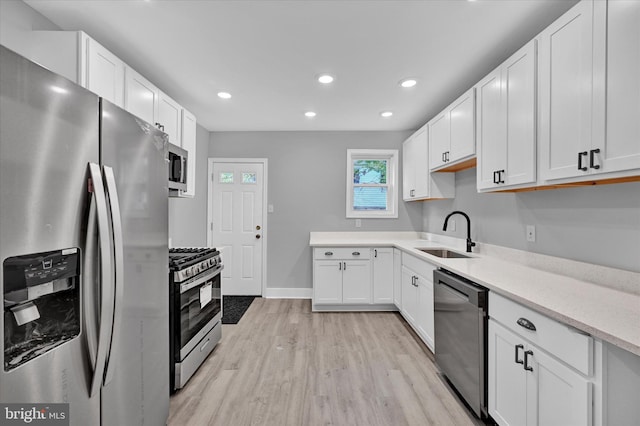 kitchen with appliances with stainless steel finishes, sink, white cabinets, and light hardwood / wood-style floors