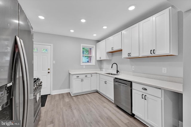 kitchen with stainless steel appliances, white cabinetry, sink, and light hardwood / wood-style flooring