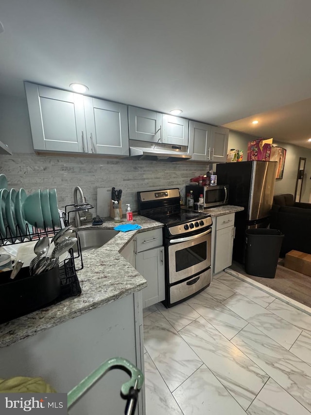 kitchen featuring sink, gray cabinetry, light stone counters, stainless steel appliances, and decorative backsplash