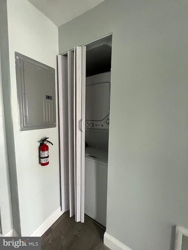 laundry area with dark wood-type flooring, stacked washer / drying machine, and electric panel