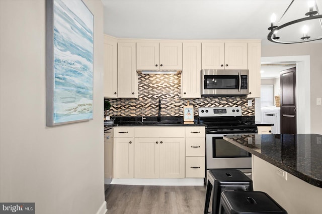 kitchen featuring sink, appliances with stainless steel finishes, dark stone countertops, backsplash, and hanging light fixtures