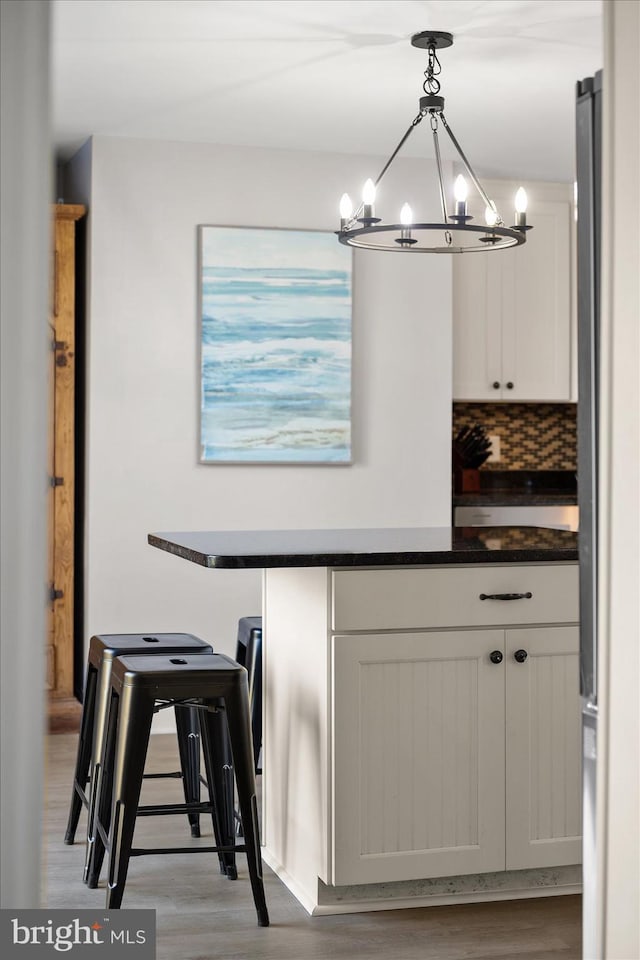 interior space featuring decorative light fixtures, white cabinets, a notable chandelier, light hardwood / wood-style floors, and backsplash