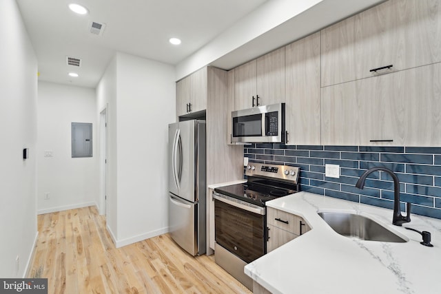 kitchen featuring appliances with stainless steel finishes, sink, decorative backsplash, light stone counters, and light wood-type flooring