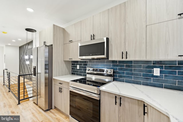 kitchen with stainless steel appliances, light brown cabinetry, light stone countertops, and light hardwood / wood-style floors