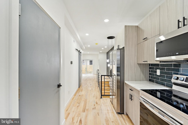 kitchen featuring light stone counters, stainless steel appliances, a barn door, light hardwood / wood-style floors, and backsplash