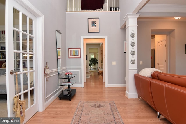 foyer featuring ornamental molding, decorative columns, a high ceiling, and light wood-type flooring