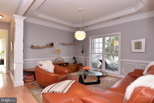 living room with ornamental molding, a tray ceiling, light hardwood / wood-style flooring, and decorative columns