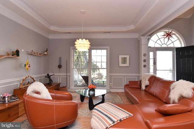 living room featuring an inviting chandelier, a tray ceiling, ornamental molding, and decorative columns