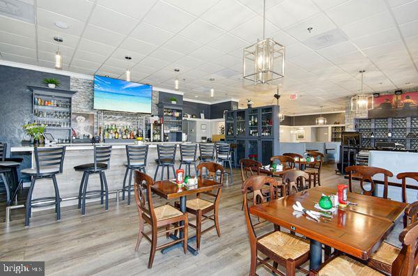 dining area featuring wood-type flooring, bar, and a drop ceiling