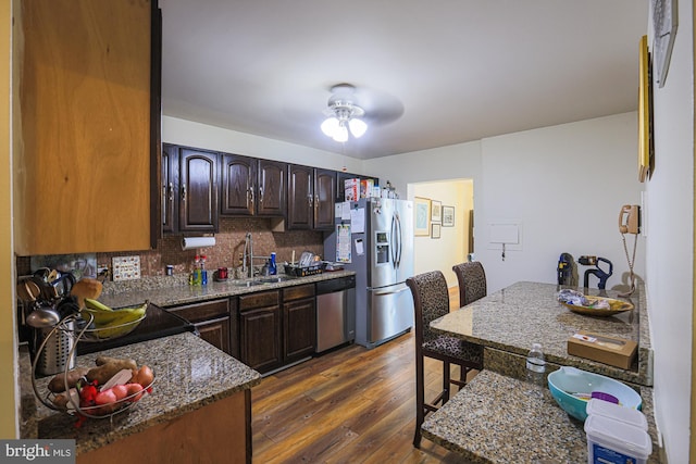 kitchen featuring dark wood-type flooring, sink, dark stone counters, stainless steel appliances, and backsplash