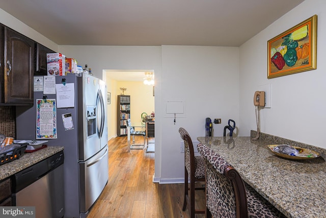 kitchen with appliances with stainless steel finishes, dark brown cabinetry, light stone countertops, and light wood-type flooring