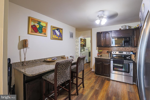 kitchen with dark wood-type flooring, washer and dryer, dark brown cabinets, dark stone countertops, and appliances with stainless steel finishes