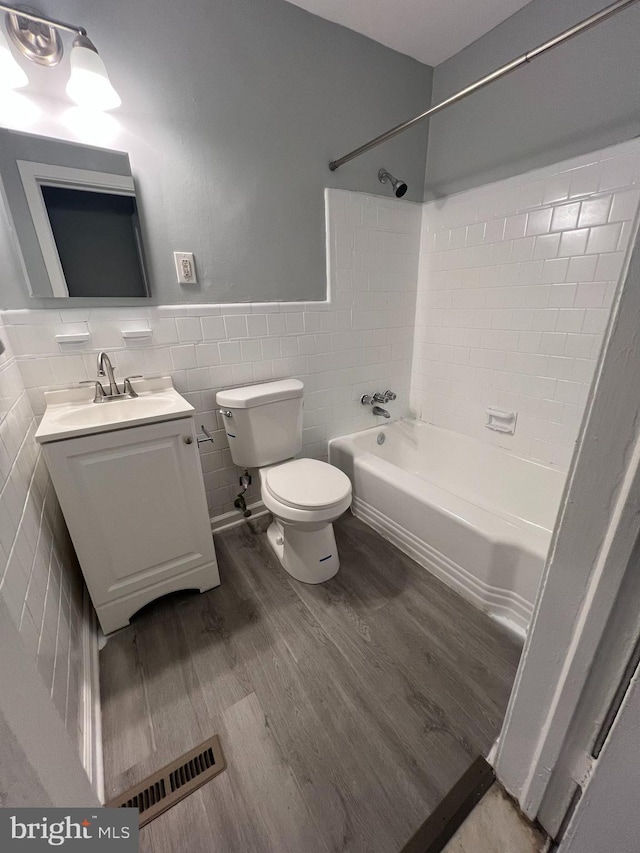 full bathroom featuring toilet, tiled shower / bath, wood-type flooring, tile walls, and vanity