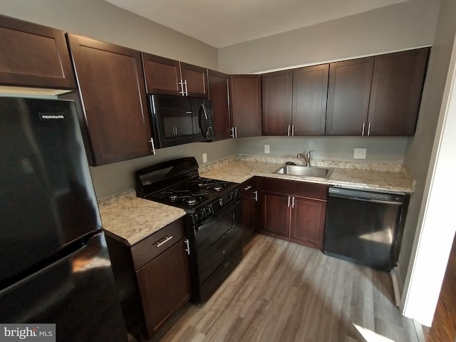 kitchen with sink, light hardwood / wood-style flooring, dark brown cabinetry, light stone counters, and black appliances