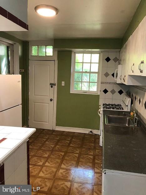 kitchen featuring dark parquet flooring, sink, tile countertops, white appliances, and decorative backsplash