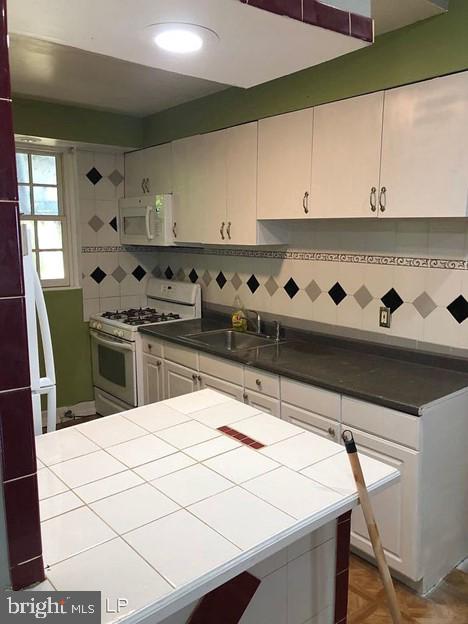 kitchen with sink, white appliances, white cabinetry, parquet flooring, and tile countertops