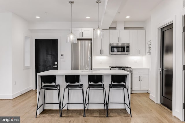 kitchen featuring stainless steel appliances, light hardwood / wood-style floors, white cabinets, a center island with sink, and decorative light fixtures