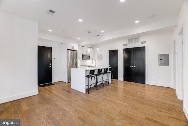 kitchen with appliances with stainless steel finishes, a breakfast bar, an island with sink, white cabinets, and hanging light fixtures