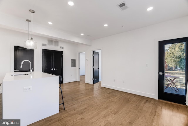 kitchen featuring decorative light fixtures, sink, a breakfast bar area, a kitchen island with sink, and light wood-type flooring