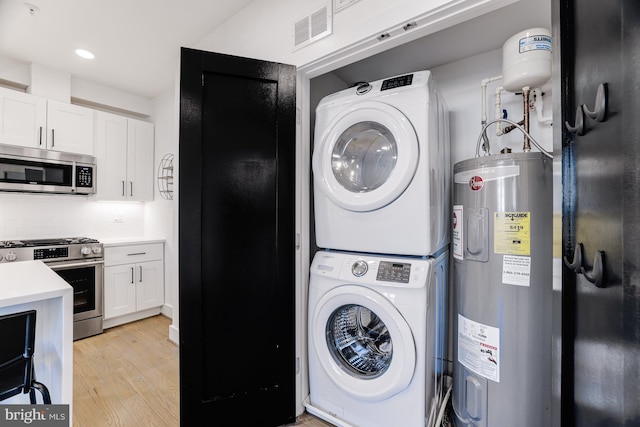 laundry room with stacked washer and clothes dryer, light hardwood / wood-style floors, and water heater