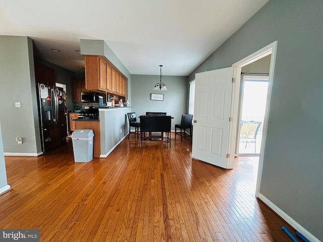 kitchen featuring hanging light fixtures, black fridge, kitchen peninsula, and light hardwood / wood-style flooring