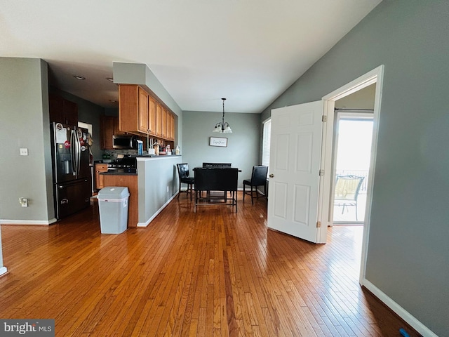 kitchen featuring pendant lighting, range, hardwood / wood-style floors, black fridge, and kitchen peninsula