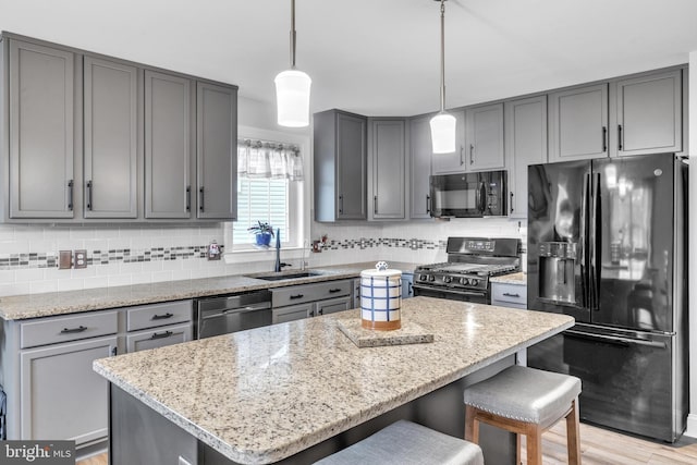 kitchen with a kitchen island, pendant lighting, sink, black appliances, and light stone countertops