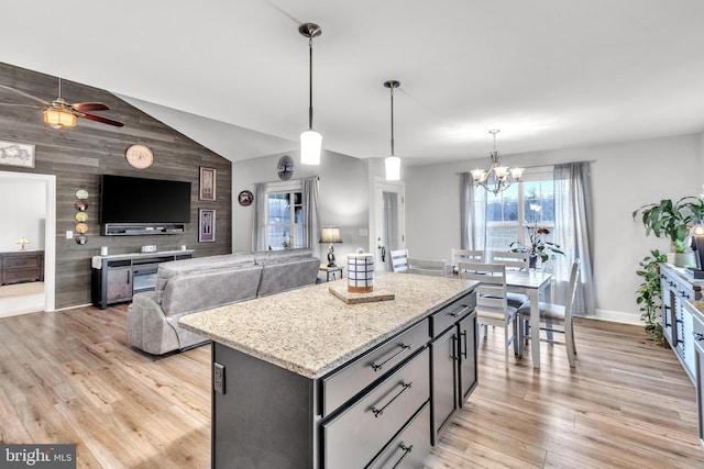 kitchen with hanging light fixtures, light hardwood / wood-style floors, light stone countertops, a kitchen island, and vaulted ceiling