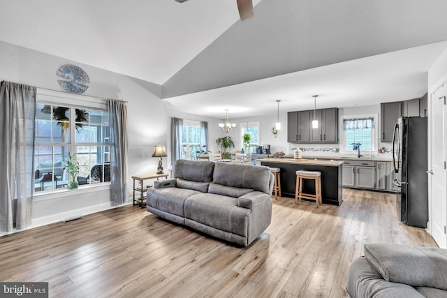 living room featuring sink, ceiling fan with notable chandelier, vaulted ceiling, and light wood-type flooring