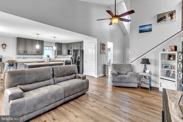 living room featuring a high ceiling, ceiling fan, and light hardwood / wood-style flooring