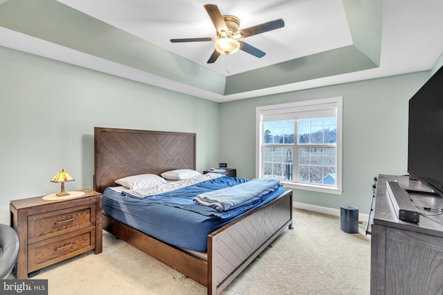 bedroom with ceiling fan, light colored carpet, and a raised ceiling