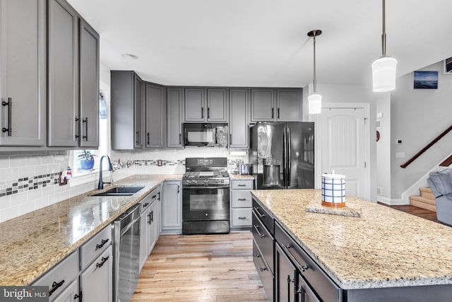 kitchen with a kitchen island, sink, hanging light fixtures, light stone counters, and black appliances