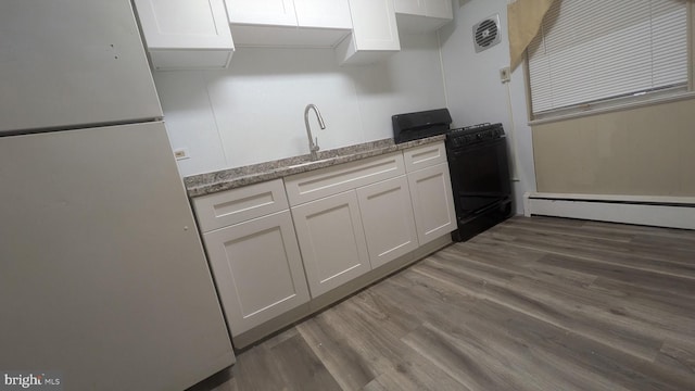 kitchen with gas stove, white refrigerator, dark hardwood / wood-style flooring, white cabinets, and baseboard heating