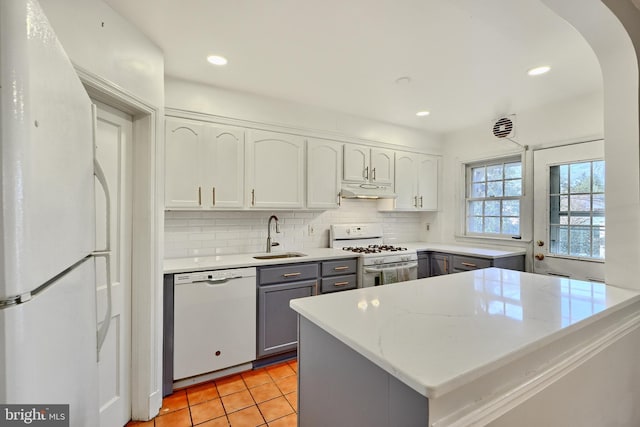 kitchen with sink, white appliances, light tile patterned floors, gray cabinetry, and tasteful backsplash