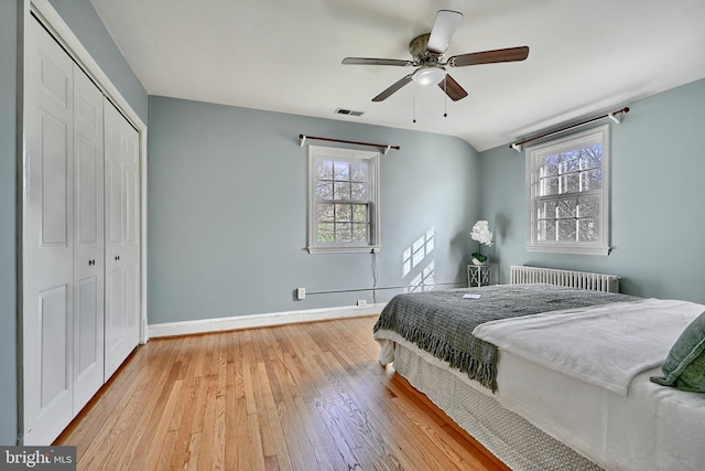 bedroom featuring ceiling fan, radiator heating unit, a closet, and light wood-type flooring