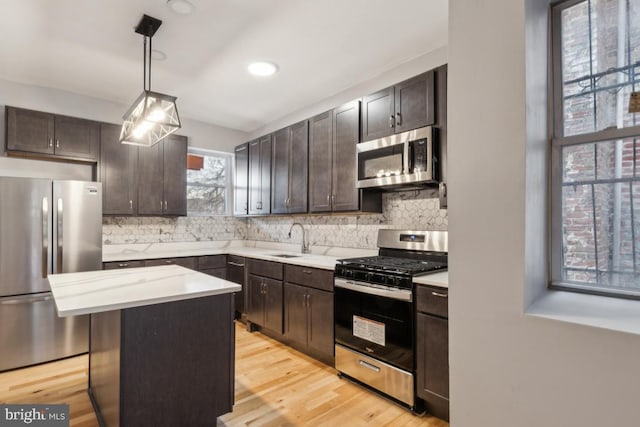 kitchen with sink, hanging light fixtures, a kitchen island, stainless steel appliances, and backsplash