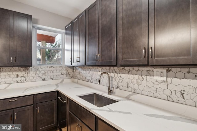 kitchen with sink, backsplash, dark brown cabinets, and light stone countertops