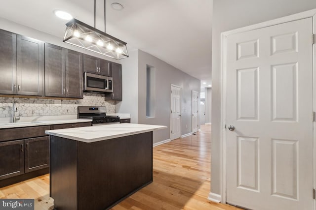 kitchen with sink, appliances with stainless steel finishes, hanging light fixtures, backsplash, and a center island