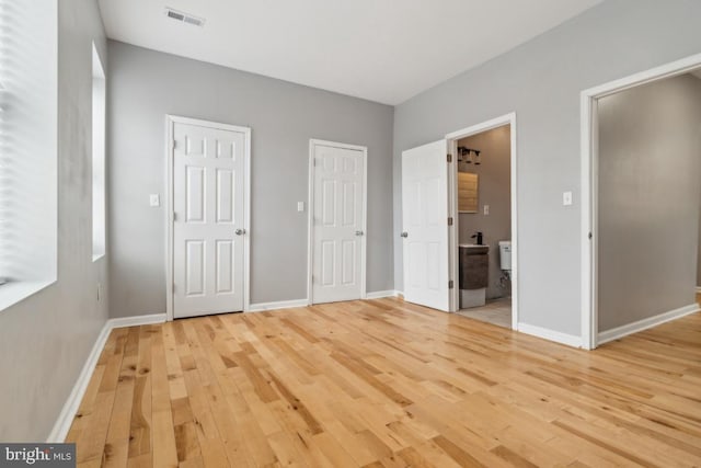 unfurnished bedroom featuring two closets, ensuite bath, and light wood-type flooring